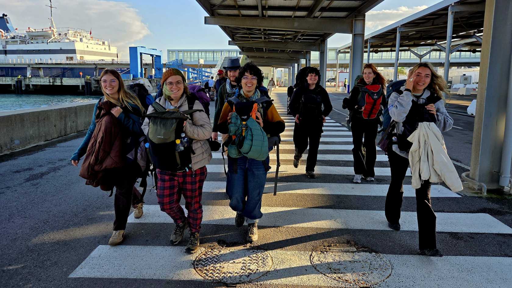 Eine Gruppe von junge Menschen ist mit Rollkoffern an einem Fährterminal unterwegs.